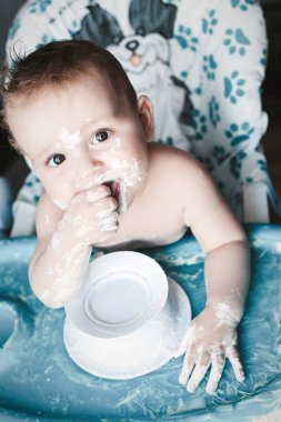 Bebek sandalyesinde oturup yoğurt tabağıyla oynadığı için çok mutlu..