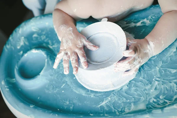 messy hands of a little baby boy without dress playing with almost empty dirty plate from yogurt