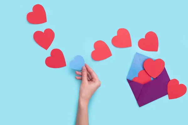 Från ett kuvert går ut en hel del rött hjärta med ett blått hjärta som flickorna handen håller i det. älskar Alla hjärtans dag den 14 februari — Stockfoto