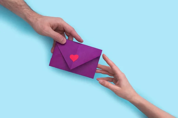 La mano del hombre da un sobre con un corazón a una mujer en la mano sobre un fondo rosa. día de San Valentín. —  Fotos de Stock