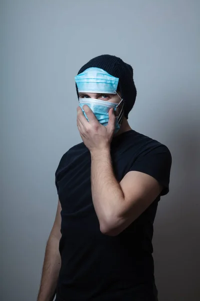 Jongeman draagt veel gezichtsbeschermende medische maskers voor bescherming tegen virusziekten op grijze achtergrond — Stockfoto