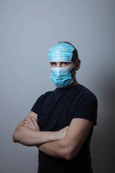 Junger Mann trägt viele medizinische Gesichtsschutzmasken zum Schutz vor Viruserkrankungen vor grauem Hintergrund — Stockfoto