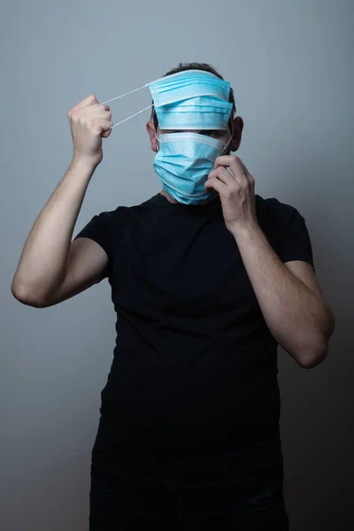 Junger Mann trägt viele medizinische Gesichtsschutzmasken für zusätzlichen Schutz vor Viruserkrankungen vor grauem Hintergrund — Stockfoto