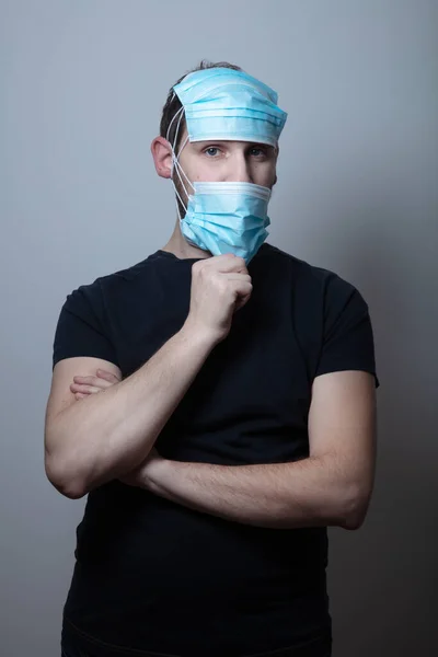 Junger Mann trägt viele medizinische Gesichtsschutzmasken für zusätzlichen Schutz vor Viruserkrankungen vor grauem Hintergrund — Stockfoto