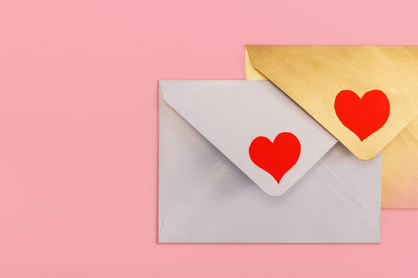 light mother-of-pearl and golden paper envelopes with red hearts isolated on pink background