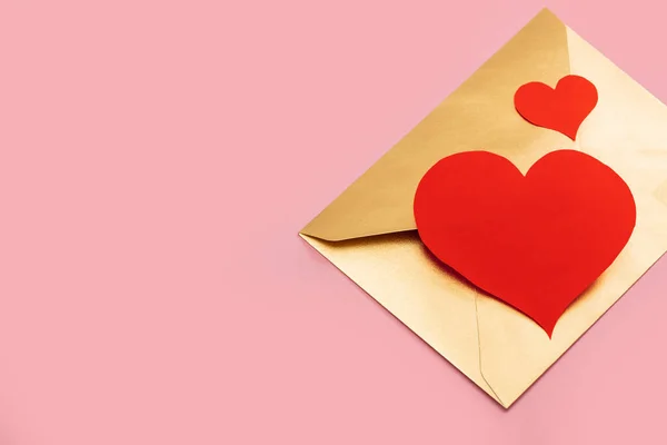 Envelope de papel dourado com dois corações vermelhos isolados sobre fundo rosa — Fotografia de Stock