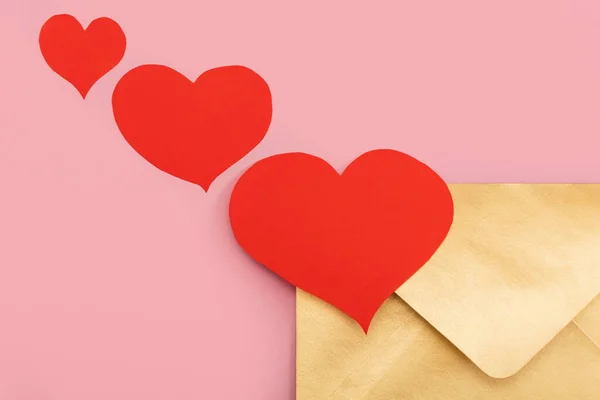 Envelope de papel dourado com corações vermelhos perto dele isolado no fundo rosa — Fotografia de Stock