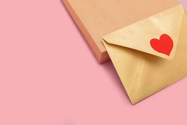 Золотистий кольоровий паперовий конверт з червоним серцем на подарунковій коробці ізольований на рожевому фоні — стокове фото