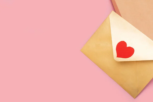Золотистий кольоровий паперовий конверт з червоним серцем на подарунковій коробці ізольований на рожевому фоні — стокове фото