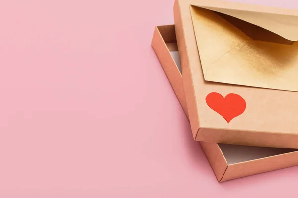 Золотистий кольоровий паперовий конверт з червоним серцем на подарунковій коробці вільний всередині ізольований на рожевому фоні — стокове фото