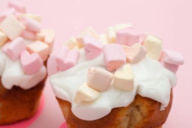 Pembe arka planda tatlı krema ve kalp şeklinde şekerlemelerle kaplı iki yeni pişmiş kekin yakın plan fotoğrafı. mesaj için yer. Sevgililer Günü