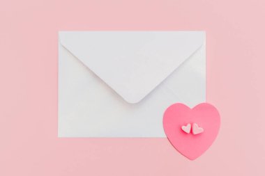 Pembe arka planda kağıt kalpli kapalı inci kokulu zarf.