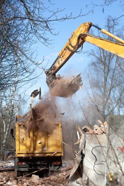 Binanın yıkımından sonra kazıcı inşaat atıklarını kamyona yüklemesine rağmen, onu alamadı. Tahtalar ve tuğlalar kamyonun gövdesine ve yere düşüyor.