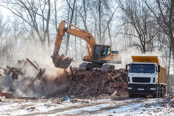 yellow excavator loading a dump truck with debris and trash after building demolition