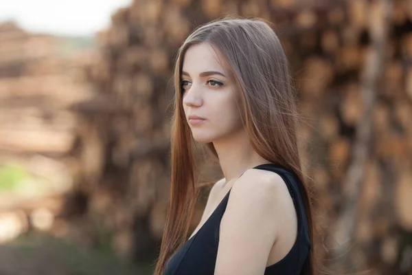 Hermosa chica en un vestido negro en el fondo de troncos cortados en el bosque —  Fotos de Stock