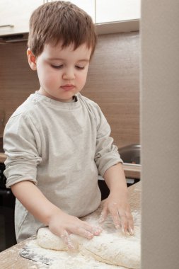 Küçük çocuk süzme peynir hamurundan lezzetli peynirli kekler yapmaya yardım eder.