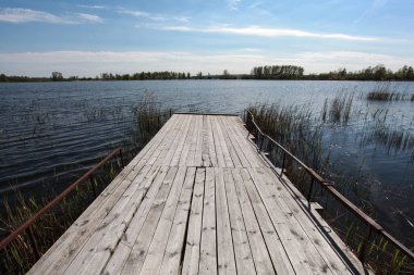 Wooden pier and grass on lake shore on sunny summer day with beautiful clouds on blue sky