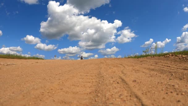 En cyklist på en cykel på bromsar kraftigt på en sandig landsväg bland fält blåser damm sand och stenar in i kameran i slow motion — Stockvideo