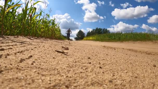 Um ciclista em uma bicicleta em freios agudamente em uma estrada rural arenosa entre campos soprando areia de poeira e pedras na câmera em câmera em câmera lenta — Vídeo de Stock
