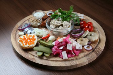 Yuvarlak bir tahtanın üzerinde çeşitli votka atıştırmalıkları.