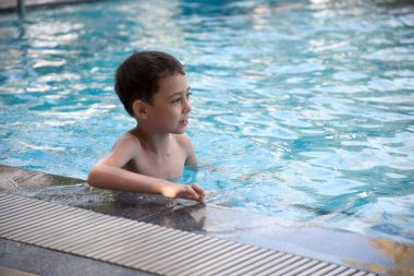Çocuk havuzun kenarında suyun içinde oturuyor.