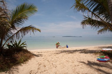 Sahilleri, palmiyeleri ve dinlenen insanları olan bir manzara.