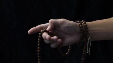 Karanlık bir arka planda el, tespihin üzerinden geçer.