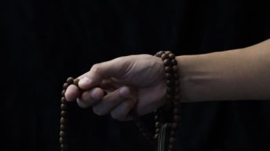 Karanlık bir arka planda el, tespihin üzerinden geçer.