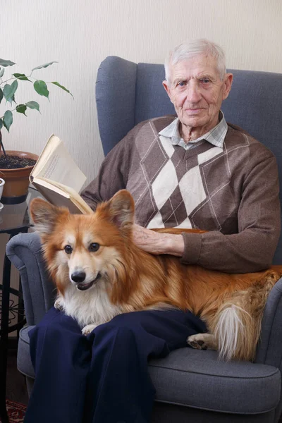 portrait of  senior man with dog corgi sitting in an armchair and reading books. leisure old ma