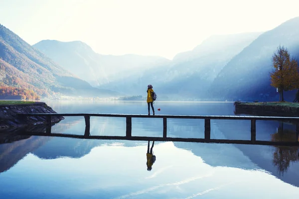 帽子を被った少女観光客とリュックを持った少女は早朝に山の湖の上の木製の橋の上に立っています 美しい風景と反射 — ストック写真