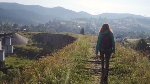 明るい夏の日に古い石造りの橋を渡って山の川を渡るハイカーの女の子 — ストック動画