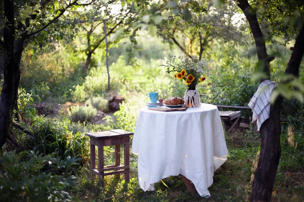 garden and tea party at the country style. still life - cinnamon rolls, cups, dishes and a vase with wildflower