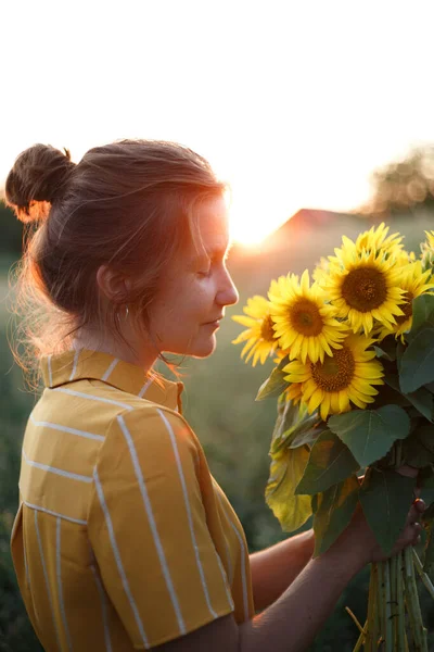 girl holding a huge bouquet of sunflowers in their hands in the sunset ligh