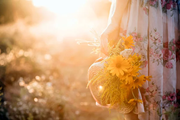 帽子をかぶった夕日の畑の女の子と野の花の花束 — ストック写真