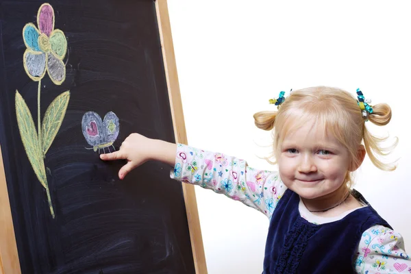 Lächelndes kleines Mädchen, das neben der Tafel steht — Stockfoto