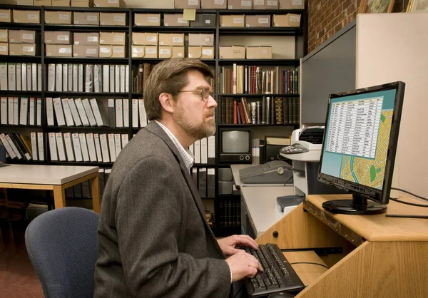 Pesquisador pesquisando um banco de dados de computador em um arquivo de biblioteca — Fotografia de Stock