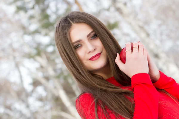 Flicka i röd klänning och med ett rött äpple på en bakgrund av en birchwood — Stockfoto