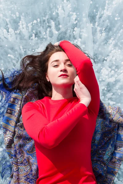 Young girl in a red dress lying on the ice of Lake Baikal — Stock Photo, Image