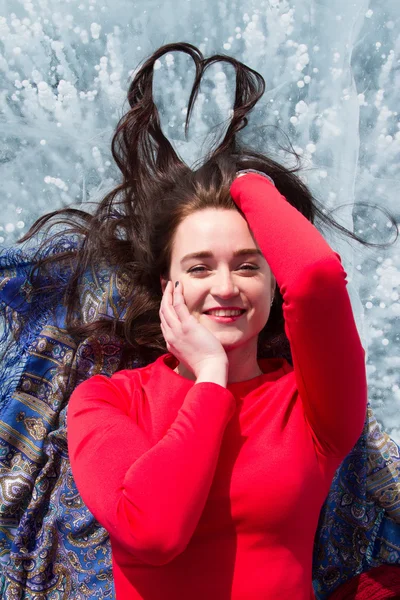 Young girl in a red dress lying on the ice of Lake Baikal — Stock Photo, Image