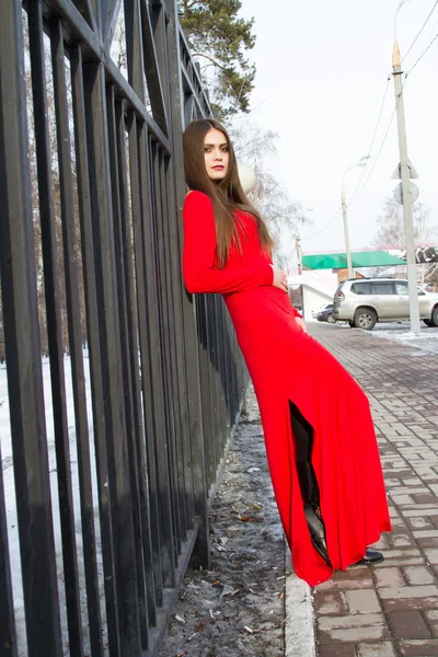 Menina em um vestido vermelho está encostado contra as cercas de metal — Fotografia de Stock