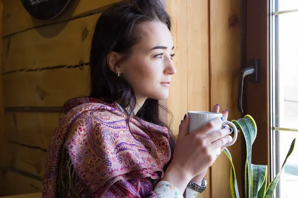 Chica joven con una taza de café de pie en la ventana — Foto de Stock