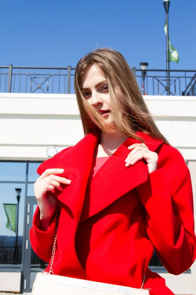 Krásná mladá dívka v červeném kabátě na pozadí kancelářská budova — Stock fotografie