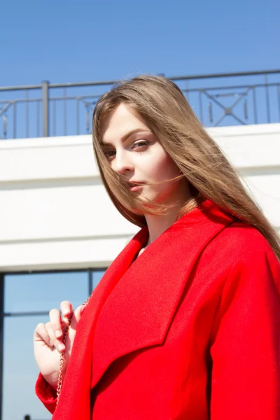 Beautiful young girl in red coat on the background of office building — Stock Photo, Image