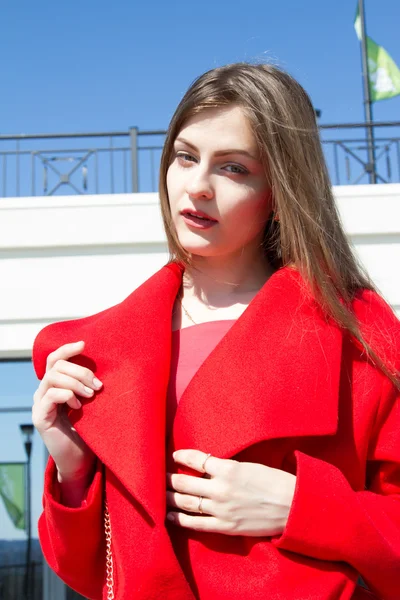 Beautiful young girl in red coat on the background of office building — Stock Photo, Image