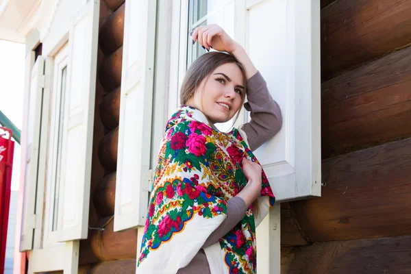 Lány egy tarka selyemkendő a háttérben az a fából készült ház — Stock Fotó