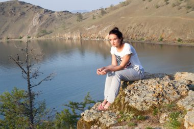 Arka planda Deniz Baykal kayalık kıyısında oturan genç kız 