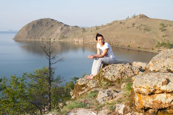 Young girl sitting on the rocky shore of Lake Baikal in the background — Stock Photo, Image