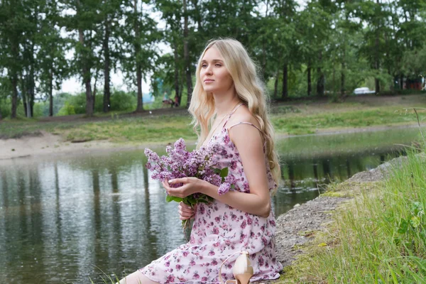 Mujer embarazada joven con un ramo de lilas en la orilla del río —  Fotos de Stock