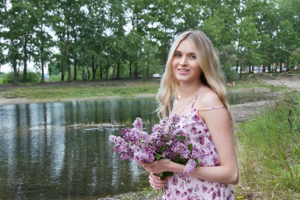 Jeune femme enceinte avec un bouquet de lilas sur la rive de la rivière — Photo