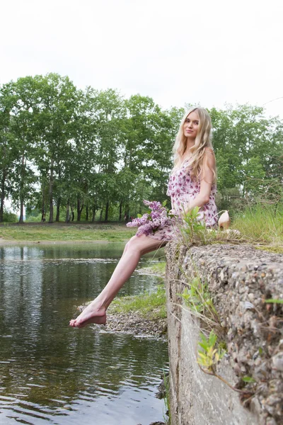 Mujer embarazada joven con un ramo de lilas en la orilla del río —  Fotos de Stock